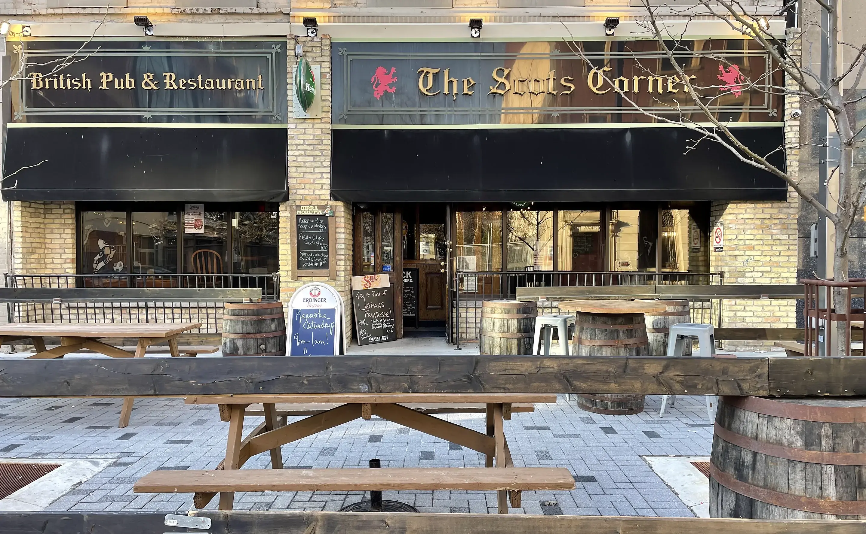 The Scot's Corner pub front on Dundas Street in London with the gold blackletter sign, red lions, black awnings and the patio with picnic tables and barrels
