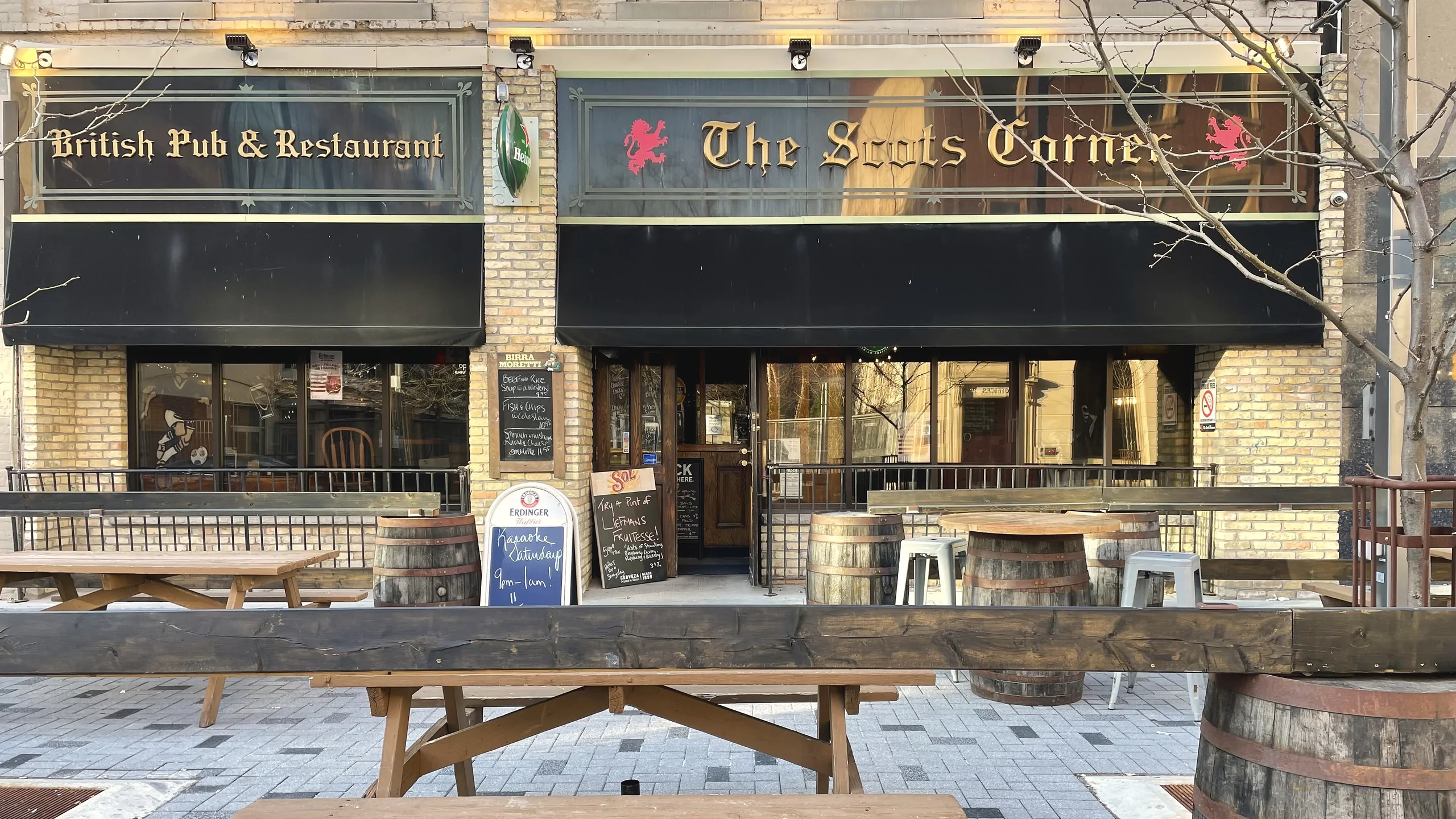 The Scot's Corner pub front on Dundas Street in London with the gold blackletter sign, red lions, black awnings and the patio with picnic tables and barrels