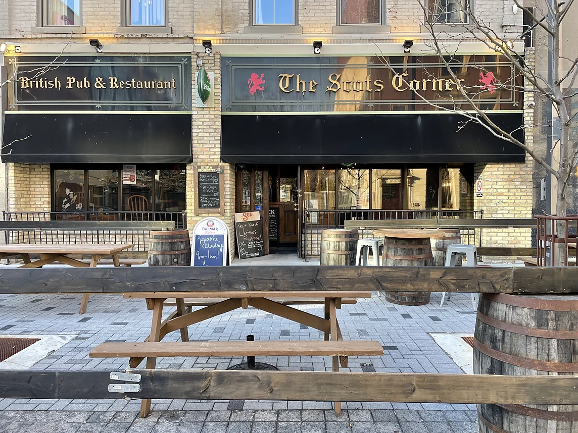 The Scot's Corner pub front on Dundas Street in London with the gold blackletter sign, red lions, black awnings and the patio with picnic tables and barrels